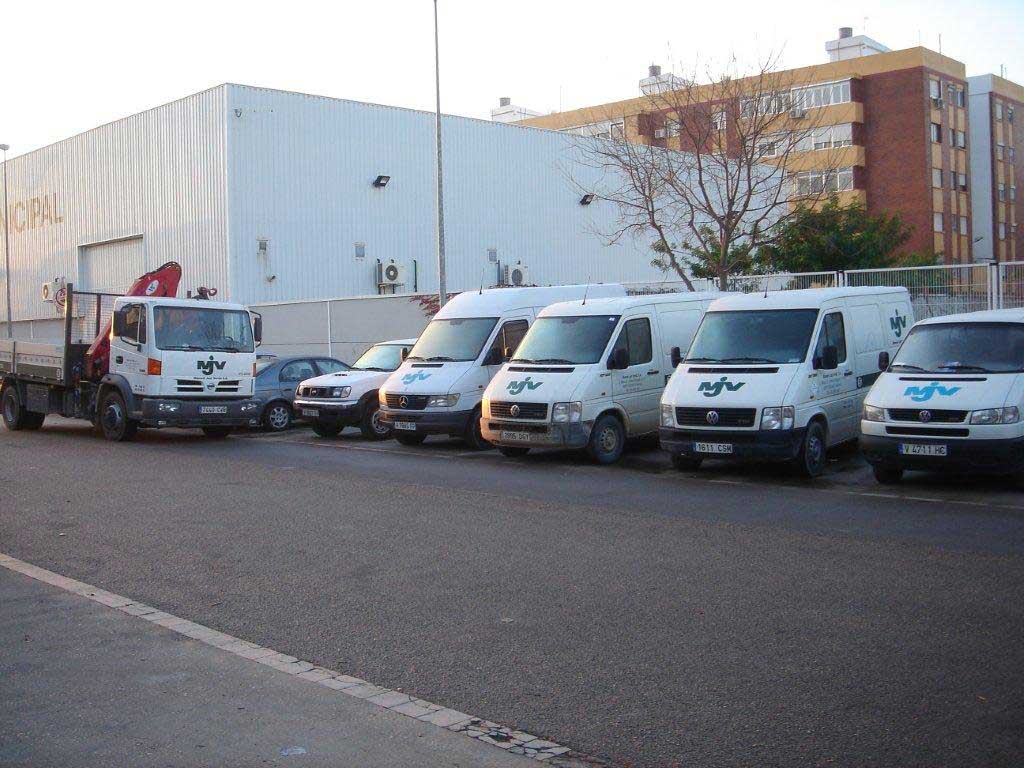 Furgonetas y camión pluma de MJV aparcados frente a la nave